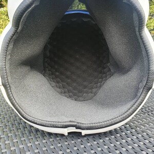 May include: A white helmet with a black interior padding. The interior padding is made of a textured, dark gray foam material. The helmet's interior is visible, showing the shape and construction of the protective headgear.