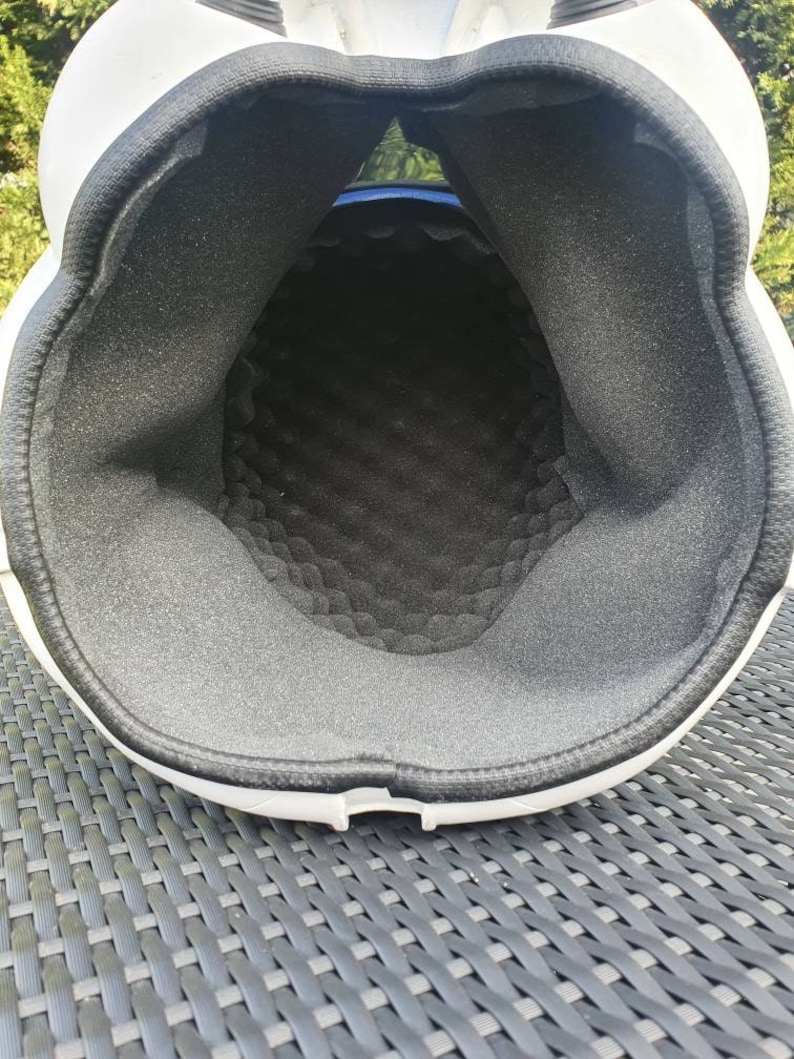 May include: A white helmet with a black interior padding. The interior padding is made of a textured, dark gray foam material. The helmet's interior is visible, showing the shape and construction of the protective headgear.