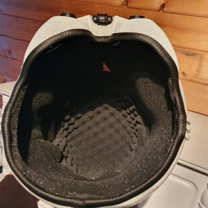 May include: White helmet with a black interior and a black rim. The inside of the helmet has a textured, foam padding. The helmet has two black circular features on the top and a black clasp.