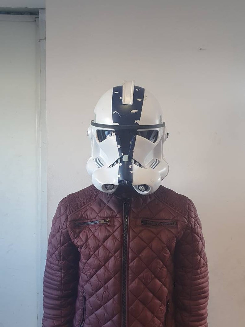 May include: A white and black helmet with a distinctive design, reminiscent of a stormtrooper. The helmet is worn over a burgundy quilted jacket with a zipper closure. The jacket has a diamond pattern.