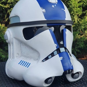 May include: A white and blue helmet with a visor and a rounded top. The helmet has blue stripes and accents, with some areas showing a distressed finish. The helmet is likely a costume piece or collectible.