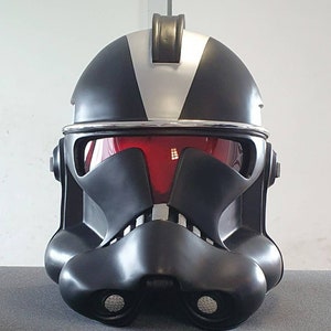 Può includere: Un elmetto di clone trooper Star Wars nero e argento con visiera rossa. L'elmetto ha una cresta distintiva sulla parte superiore.