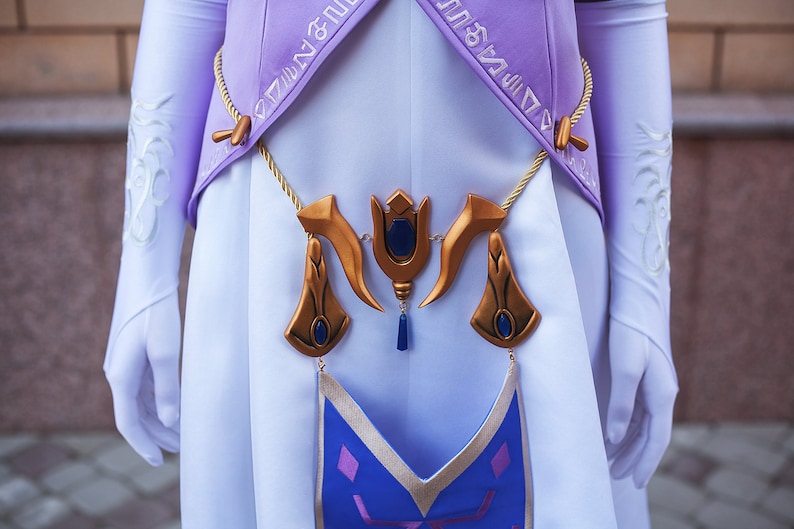 May include: A white and purple costume with a gold and blue decorative belt. The belt has a blue gem in the centre and two gold horns on either side.