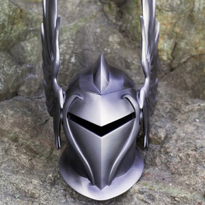 May include: A silver knight helmet with a pointed top and winged accents. The helmet has a face shield with a pointed opening for the eyes.