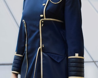 Op de afbeelding: Een donkerblauw jasje in militaire stijl met een hoge kraag, gouden biezen en een decoratieve gouden ketting op de borst. Het jasje heeft gestructureerde schouderstukken, lange mouwen met geribbelde donkerblauwe boorden en gouden sluitingen.