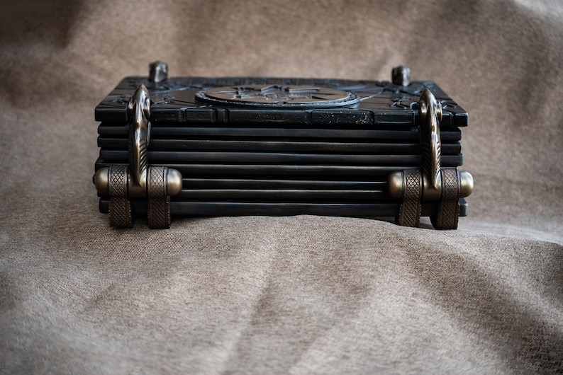 Puede incluir: Un libro encuadernado en cuero negro con cierres de metal adornados y un dise&ntilde;o decorativo en la portada.