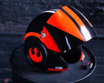 May include: A black and orange pilot helmet featuring a prominent Rebel Alliance symbol on the side. The helmet has a glossy finish, a retractable visor, and small mechanical details near the chin strap area, showcasing a bold color scheme.