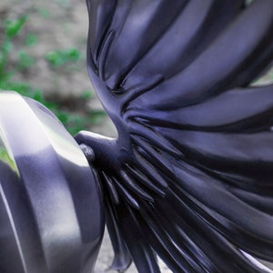 May include: A black helmet with a large, detailed wing design on the side. The wing is made of a smooth, shiny material and has a textured, feathered look.