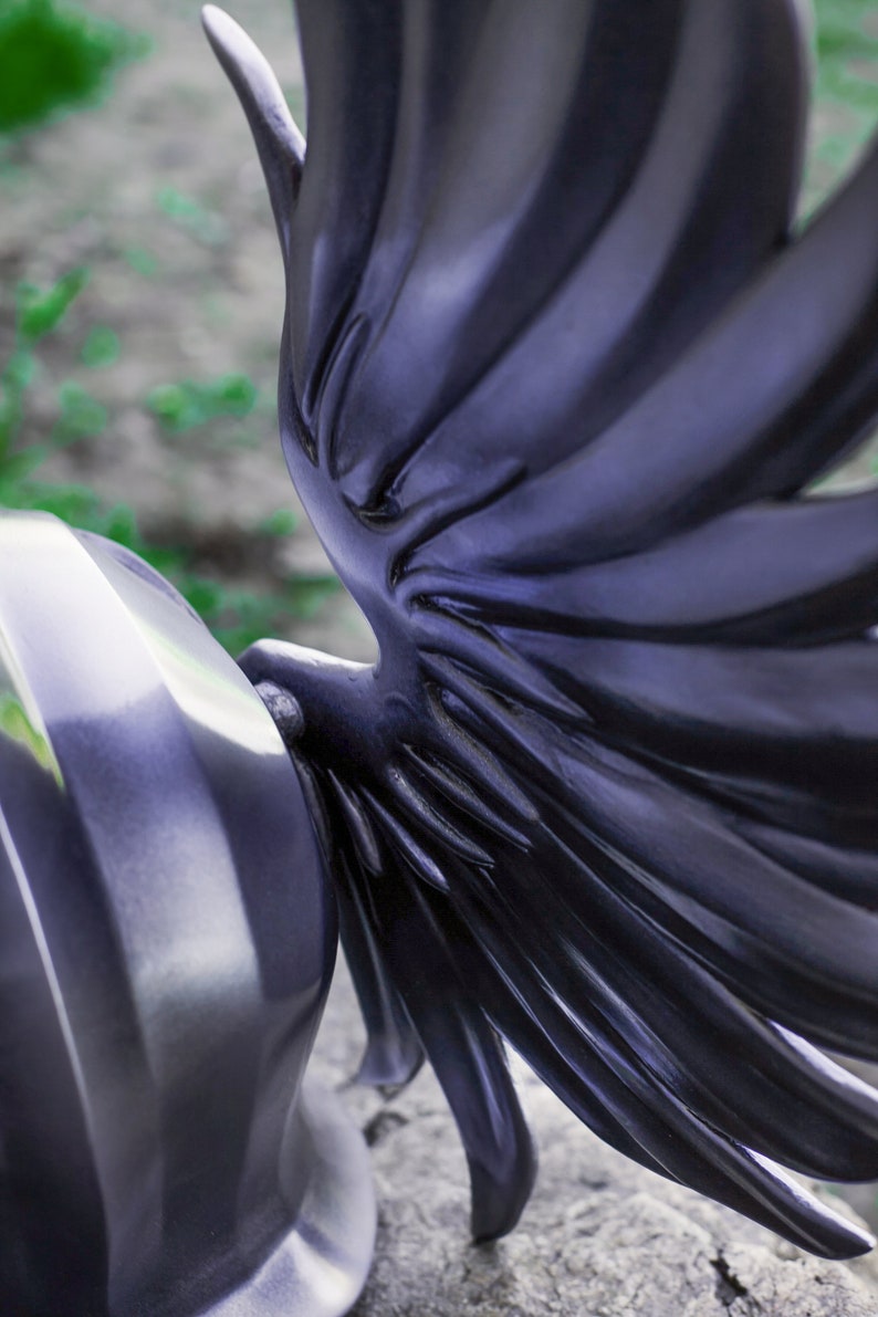 May include: A black helmet with a large, detailed wing design on the side. The wing is made of a smooth, shiny material and has a textured, feathered look.