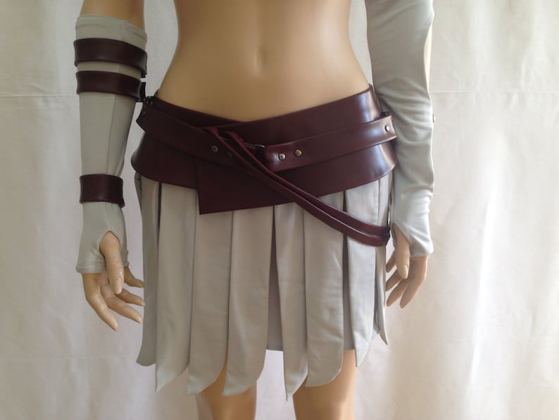 May include: A light gray pleated skirt with a wide, dark burgundy faux leather belt featuring silver-tone metal studs. The set includes matching light gray arm warmers with dark burgundy faux leather straps and silver-tone metal buckles.