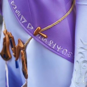 May include: A purple and white costume with gold rope and a gold pendant with blue accents. The costume has white embroidery with symbols on the sleeve and the bodice.