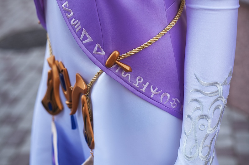 May include: A purple and white costume with gold rope and a gold pendant with blue accents. The costume has white embroidery with symbols on the sleeve and the bodice.