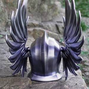 May include: A silver helmet with two large wings on the sides. The helmet is made of metal and has a smooth, polished finish.
