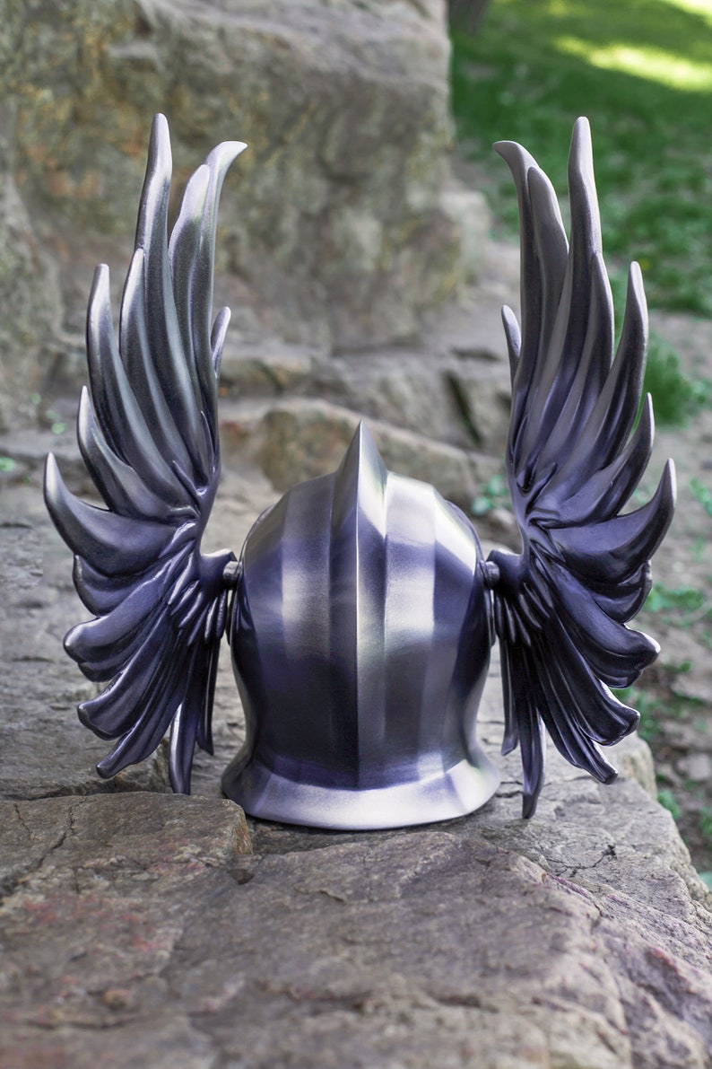 May include: A silver helmet with two large wings on the sides. The helmet is made of metal and has a smooth, polished finish.