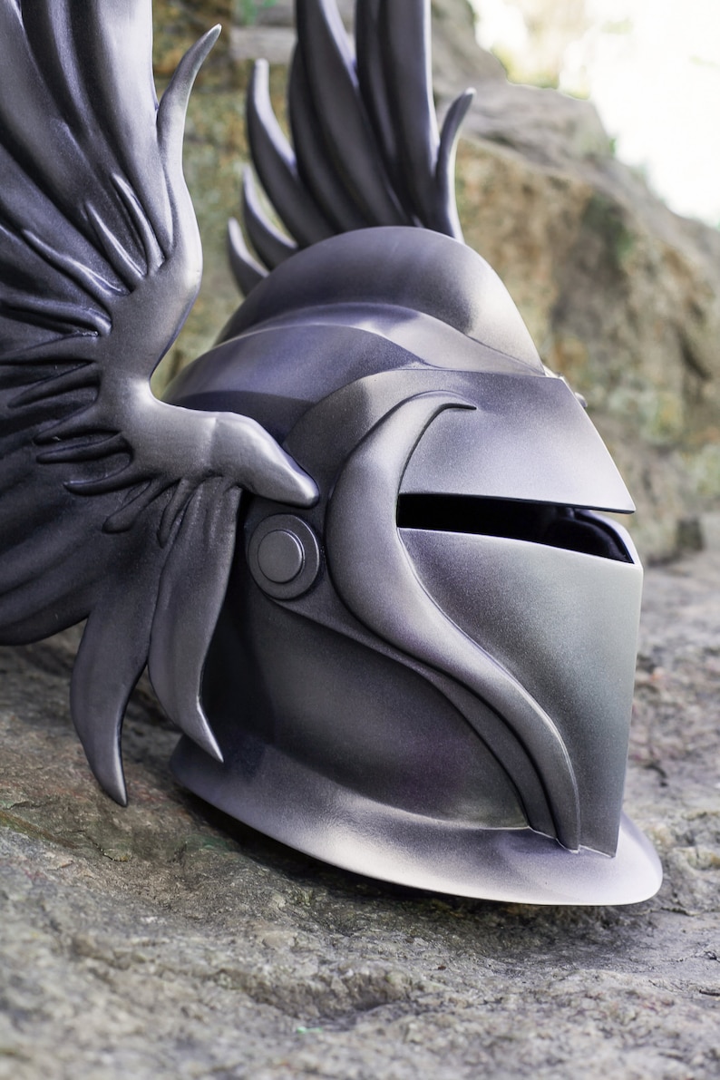 May include: A silver helmet with a winged design. The helmet has a visor and a textured surface.