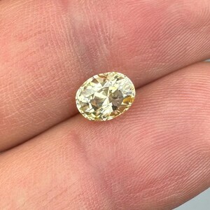 以下が含まれることがあります： 楕円形にカットされた、薄い黄色の宝石。 宝石は手で持たれており、その透明度と輝きを示しています。 石のカットにより光が反射し、キラキラとした効果を生み出しています。 宝石はジュエリー用である可能性が高いです。