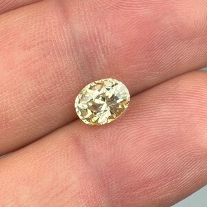 以下が含まれることがあります： ファセット加工された、楕円形のイエローダイヤモンドの宝石。 ダイヤモンドは人の手で持たれており、その輝きと透明度を示しています。 宝石のカットにより光が反射し、きらめく効果を生み出します。