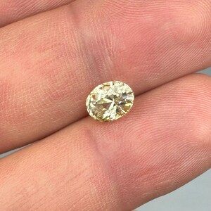 以下が含まれることがあります： 淡い黄色のオーバルカットダイヤモンド。宝石は指の間に挟まれ、そのファセットと輝きを際立たせています。ダイヤモンドの色は淡く温かみのある黄色で、カットが良く、光を反射しているようです。全体的な印象は、高品質の宝石です。