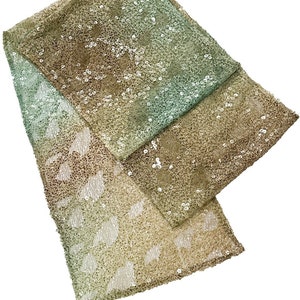 May include: A green, brown, and gold sequined fabric with a gradient effect. The fabric is folded in half and has a soft, shimmery texture.