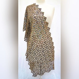 May include: A gold sequined shawl with a geometric pattern. The shawl is draped over a white mannequin.