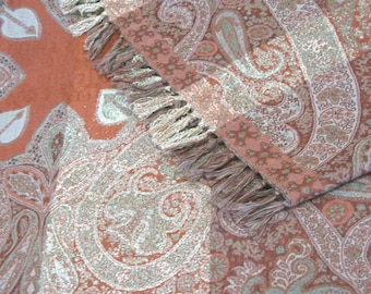 May include: A soft, peach-colored throw blanket with a paisley pattern in silver and white. The blanket has a fringe border.