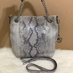 Puede incluir: Bolso de mano gris y blanco con estampado de piel de serpiente, con correas de cadena plateadas y una correa de hombro desmontable. El bolso presenta un charm con el logo MK plateado, ideal para el uso diario.