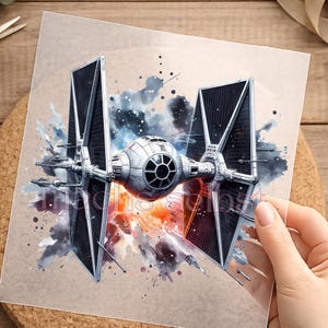 Könnte beinhalten: Ein quadratischer Druck, der ein TIE-Jäger-Raumschiff im Aquarellstil zeigt. Das Schiff ist grau mit schwarzen Solarpaneelen und vor einem Hintergrund aus dunkelblauen, schwarzen und orangefarbenen Farbspritzern platziert. Der Text "machis selpst" ist sichtbar.