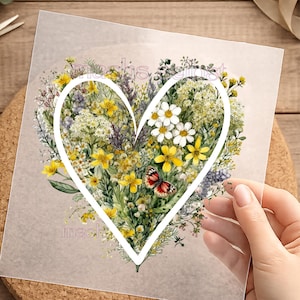 Könnte beinhalten: Ein herzförmiges Blumendesign mit gelben, weißen und lila Wildblumen und einem rot-schwarzen Schmetterling. Das Design befindet sich auf einem transparenten Blatt mit dem Text "machs gifts".