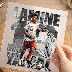 Könnte beinhalten: Ein quadratischer Grafikdruck mit einem Fußballspieler im weißen Trikot mit der Nummer 19 und roten Shorts, der über einem Fußball steht. Der Hintergrund zeigt den Text LAMINE YAMAL in großen Blockbuchstaben über einer Graustufen-Illustration.
