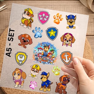 Könnte beinhalten: Ein A5-Set mit Paw Patrol-Aufklebern auf einer transparenten Folie, das verschiedene Zeichentrick-Hundecharaktere, bunte Abzeichen und Pfotenabdrücke zeigt. Das Blatt enthält einzelne Illustrationen von Charakteren wie Chase, Marshall, Rubble und Skye sowie eine zentrale Gruppenabbildung.
