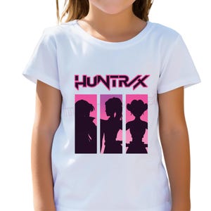 Könnte beinhalten: Weißes T-Shirt mit dem Wort "HUNTRAX" in Pink und Lila, über drei Silhouetten von Frauen vor rosa und lila Rechtecken. Die Silhouetten haben unterschiedliche Frisuren.