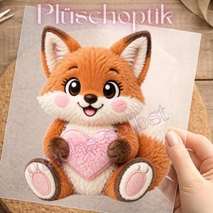 Könnte beinhalten: Ein Plüschfuchs mit orangefarbenem und weißem Fell, großen dunklen Augen und rosa Wangen, der ein weiches rosa Herz hält. Der Fuchs hat braune Pfoten und weiß gepolsterte Füße. Der Text Plüschoptik und machs selbst ist auf dem Bild gedruckt.