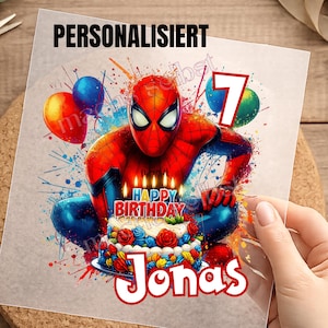 Könnte beinhalten: Ein quadratischer Grafikdruck mit einem rot-blauen Superhelden, der hinter einer Geburtstagstorte mit brennenden Kerzen kauert. Der Text lautet PERSONALISIERT, HAPPY BIRTHDAY und Jonas, ergänzt durch eine große 7 und bunte Luftballons.