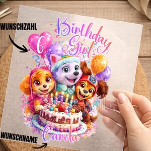 Könnte beinhalten: Ein transparentes Blatt mit einer bunten Illustration von drei Zeichentrickwelpen um eine Geburtstagstorte mit brennenden Kerzen. Der Text lautet Birthday Girl und Carola, mit WUNSCHZAHL und WUSCHNAME Beschriftungen für die Bereiche.