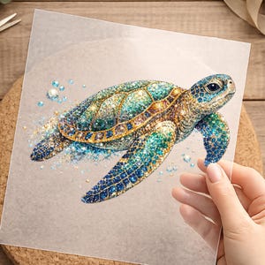 Könnte beinhalten: Ein quadratisches, transparentes Blatt mit einer detaillierten Grafik einer Meeresschildkröte. Die Schildkröte ist in leuchtenden Blau-, Grün- und Goldtönen mit einer funkelnden, strukturierten Oberfläche dargestellt. Kleine blaue und weiße kreisförmige Akzente umgeben die Schildkröte.