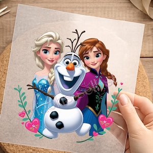 Könnte beinhalten: Eine transparente Folie mit einer farbenfrohen Grafik von Elsa mit blondem Haar in einem blauen Kleid, Anna mit geflochtenem rotbraunem Haar in einem violett-schwarzen Outfit und dem Schneemann Olaf, umgeben von grünen Zweigen und rosa Herzen.