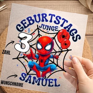Könnte beinhalten: Ein transparenter Aufkleber mit einer Spider-Man-Comicfigur im rot-blauen Anzug, zentriert in einem schwarzen Spinnennetz. Der Text lautet GEBURTSTAGS JUNGE, die Zahl 3 und der Name SAMUEL, ergänzt durch rote Luftballons und Konfetti.