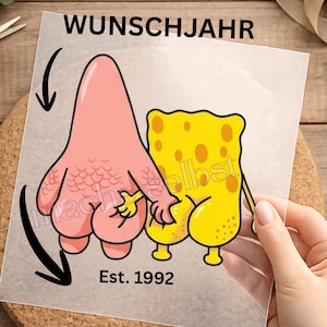 Könnte beinhalten: Ein transparenter Aufkleber mit einer Cartoon-Illustration eines rosa Seesterns und einer gelben Schwammfigur, die nebeneinander stehen. Der Text WUNSCHJAHR steht oben und Est. 1992 unten. Zwei schwarze Pfeile zeigen auf die Figuren.