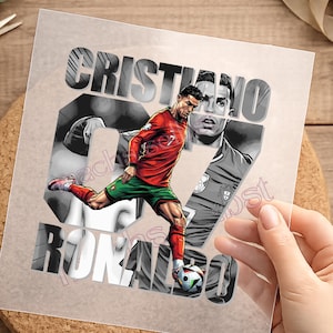 Könnte beinhalten: Eine transparente Transferfolie mit einer Grafik von Cristiano Ronaldo im roten Trikot und grüner Hose, der einen Fußball kickt. Das Design enthält den Text CRISTIANO RONALDO in großen, fetten Buchstaben und ein Graustufen-Porträt des Sportlers.