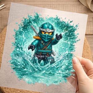 Könnte beinhalten: Eine Grafik einer türkisfarbenen Ninja-Figur auf einer transparenten Folie, die einen maskierten Charakter mit gelben Augen zeigt, umgeben von einem dynamischen Spritzer türkisfarbenen Wassers. Ein Schwertgriff ist hinter der Schulter sichtbar.