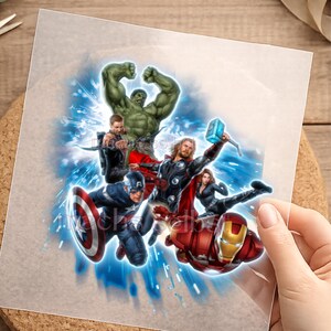 Könnte beinhalten: Eine transparente Transferfolie mit einer lebendigen Grafik der Marvel Avengers-Charaktere, darunter Hulk, Thor, Iron Man, Captain America, Black Widow und Hawkeye. Das Design ist vor einem dynamischen blauen Energiehintergrund platziert.