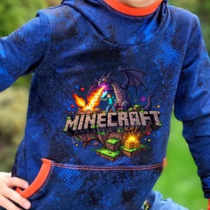 Könnte beinhalten: Blauer Kapuzenpullover mit einem Minecraft-Motiv. Das Design zeigt einen Drachen, der Feuer auf eine Minecraft-Figur speit. Das Wort "Minecraft" ist prominent dargestellt. Der Kapuzenpullover hat eine orange gefütterte Kapuze und Tasche.