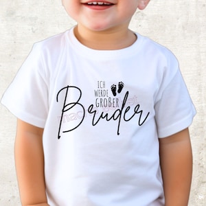 Könnte beinhalten: Weißes Kurzarm-T-Shirt mit dem Text "Bruder" in Schreibschrift. Über dem Wort "Bruder" stehen die Worte "Ich werde groBer" und zwei kleine Fußabdrücke. Das T-Shirt wird von einem Kind getragen.