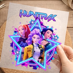 Könnte beinhalten: Eine transparente Transferfolie mit dem Text "HUNTRX" in einem violett-blauen Farbverlauf über drei animierten Figuren, die von einem neonblauen Stern eingerahmt sind. Das Design enthält violette und blaue Farbspritzer und kleine Sterne.