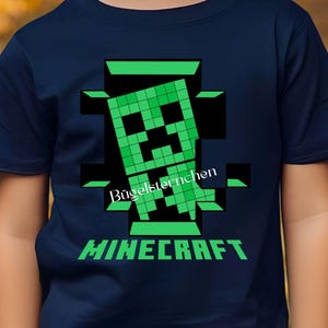 Könnte beinhalten: Marineblaues T-Shirt mit einem pixeligen grünen Creeper-Design aus Minecraft. Das Wort "MINECRAFT" ist unter der Grafik grün gedruckt. Der Text "Bügelsternchen" ist über der Grafik gedruckt.