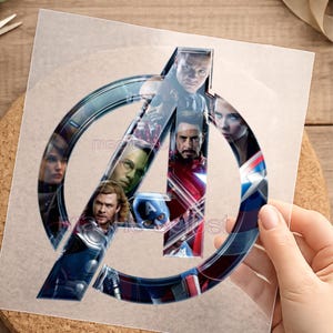 Könnte beinhalten: Ein transparenter Aufkleber mit dem Avengers-Logo und Bildern der Charaktere. Das Logo ist ein großes, stilisiertes "A" mit blau-silberner Umrandung. Die Bilder der Charaktere sind im Logo sichtbar.