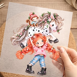 Könnte beinhalten: Eine farbenfrohe Illustration auf einer transparenten Folie zeigt eine rothaarige Figur in einem rosa Pullover und einer zerrissenen blauen Jeans, die ein weißes geflecktes Pony hochhebt, auf dessen Rücken ein Äffchen mit rosa Mütze sitzt.