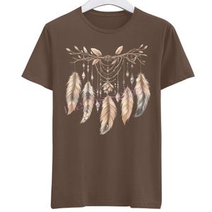 Könnte beinhalten: Braunes T-Shirt mit einem Traumfänger-Design. Das Design zeigt Federn in Beige-, Braun- und Grautönen, hängende Kristalle und Perlen. Das T-Shirt hat einen Rundhalsausschnitt.