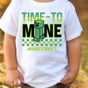 Könnte beinhalten: Weißes T-Shirt mit dem Text "TIME-TO MINE" in Grün und Schwarz, mit einer pixeligen grünen Figur. Das Wort "MINECRAFT" steht darunter. Das T-Shirt wird von einem Kind getragen.
