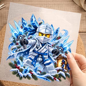 Könnte beinhalten: Ein grafischer Aufkleber mit einer weiß-blauen Ninja-Figur, die zwei leuchtend blaue Eisklingen hält. Die Figur trägt eine weiße Maske und einen Anzug mit einer blauen Schärpe und dem Buchstaben N auf der Brust. Das Design umfasst blaue Kristalle, Schneeflocken und Tannenzweige mit roten Beeren.